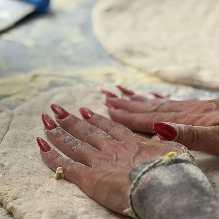 Mani che stendono l'impasto sul banco infarinato