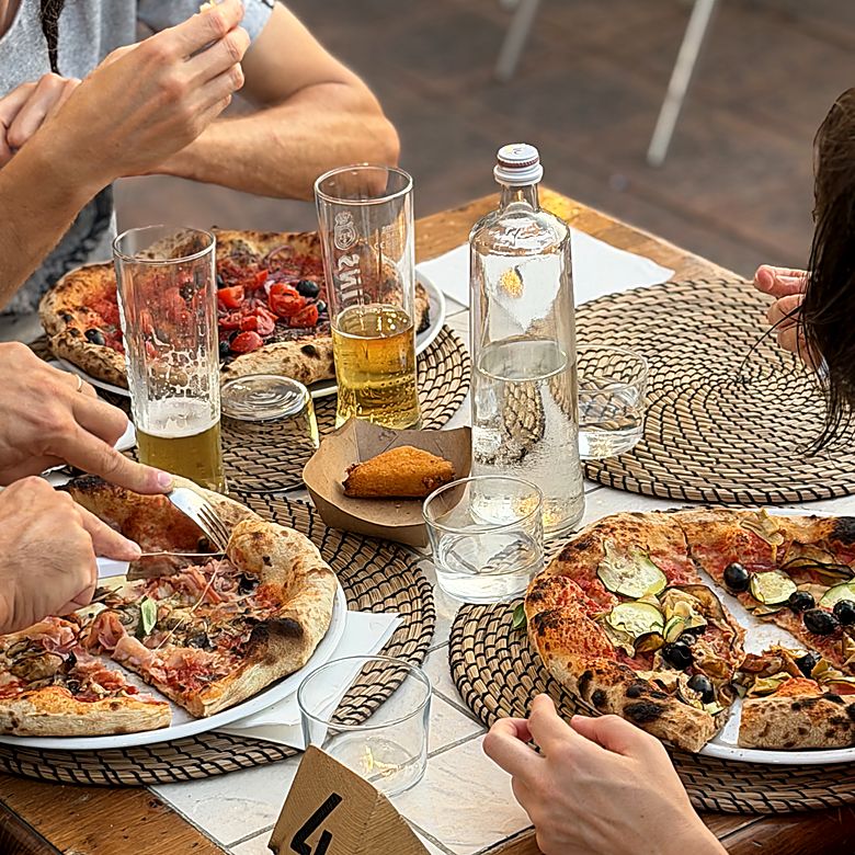 Tre pizze in tavola con birre e acqua, viste dall'alto